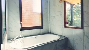 Un baño con bañera, ventana y piso de piedra.