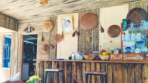 Un interior rústico con mostrador de madera que dice "Fruit Smoothie", cestas y maceteros tejidos en la pared.