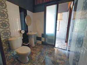 Casa de banho com sanita, lavatório e espelho. O chão tem um padrão de mosaicos.