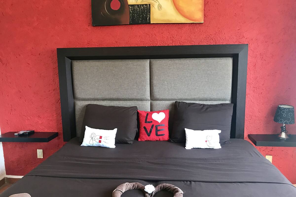 Una cama con una toalla con forma de corazón, dos almohadas con la palabra 'LOVE' y un cuadro en la pared.