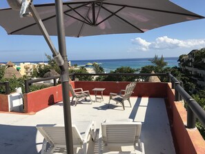 A balcony with a view of the sea, a table, two chairs, and an umbrella. - Embarcadero Maya B&B (Playa del Carmen)