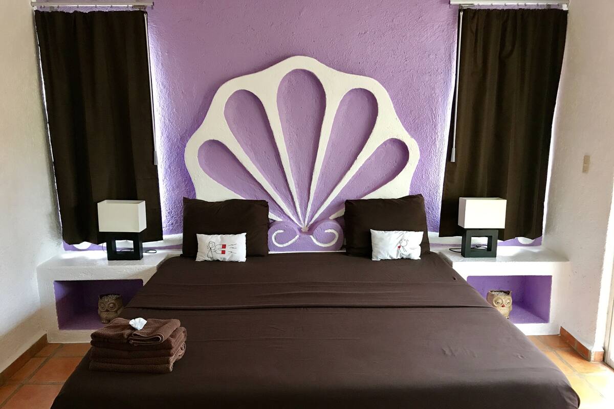 Una cama con un cabecero grande, dos mesitas de noche con lámparas y una pila de toallas.