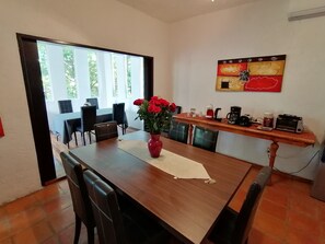 A dining area with a wooden table, chairs, a vase of red flowers, and a kitchen counter with appliances. - Embarcadero Maya B&B (Playa del Carmen)