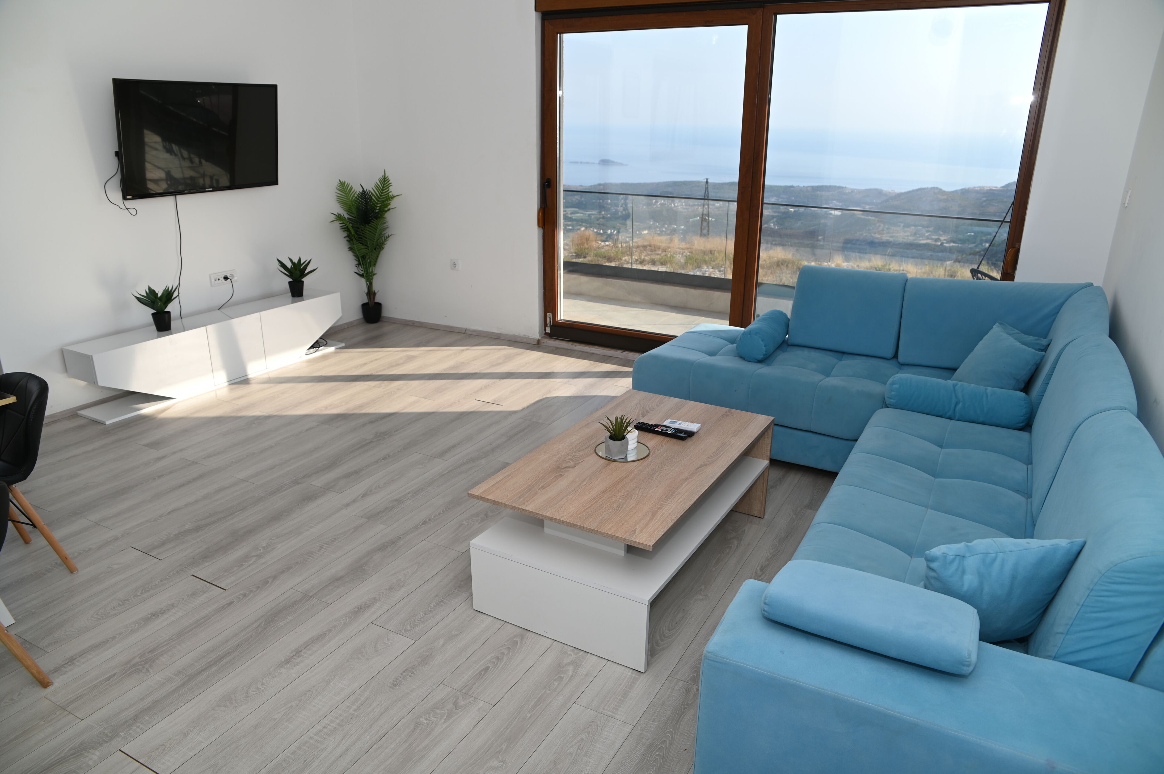 Een moderne woonkamer met een blauwe bank, een salontafel en een aan de muur bevestigde televisie.