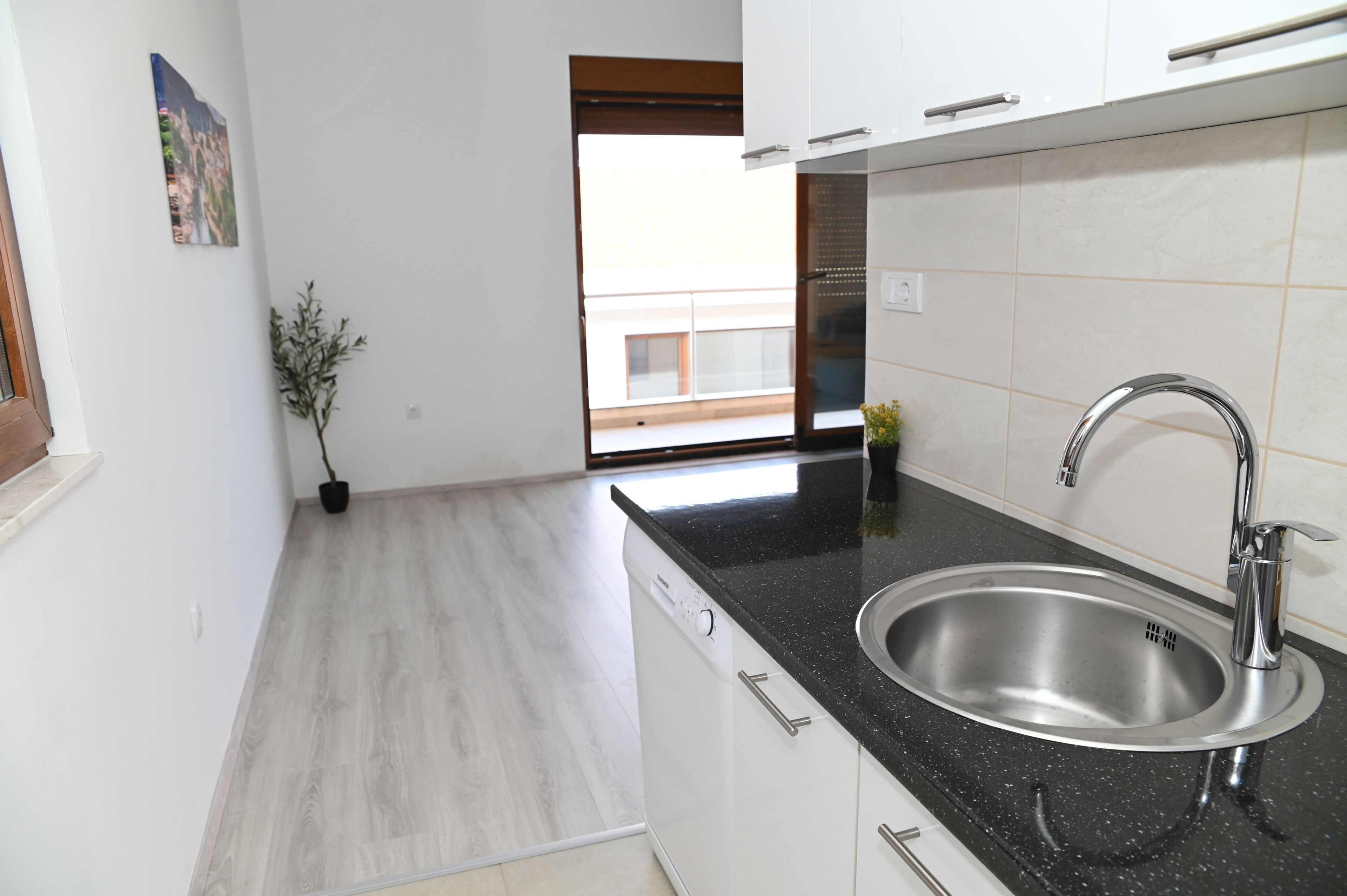 A modern kitchen with a stainless steel sink, black countertop, and white cabinets.