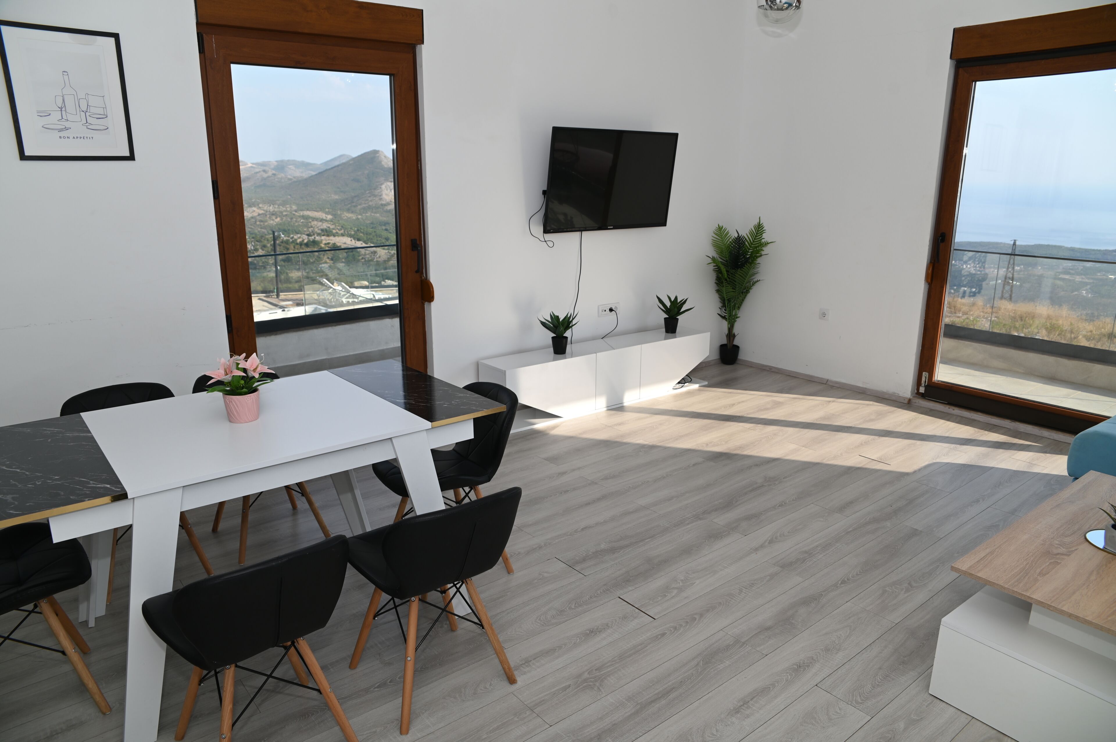 Un espace repas moderne avec une table blanche, des chaises noires et une vue sur l’extérieur.