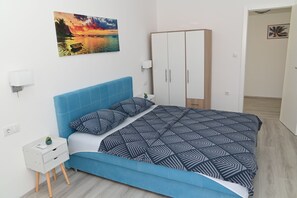 A bedroom with a bed, a wardrobe, a nightstand, a wall-mounted lamp, and a painting.