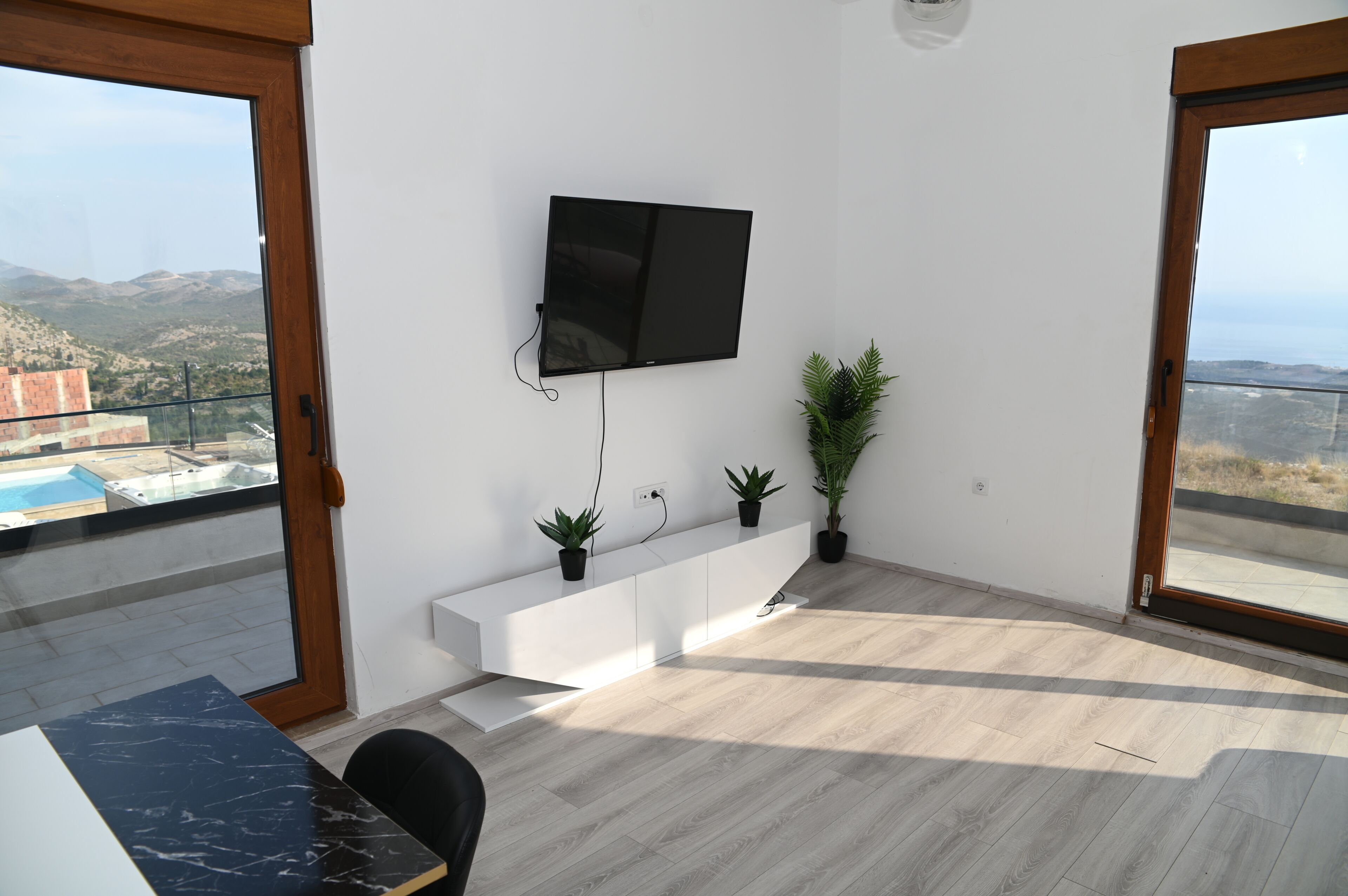 Uma sala de estar moderna com uma TV de tela plana na parede, um console branco e duas plantas em vasos.