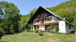 A two-story chalet with a balcony, surrounded by lush greenery and a sloped roof. - Molliessoulaz barn with wolves (Queige)