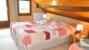 A bed with a quilt, two bedside lamps, a small table with a tablecloth, and a window with curtains. - Molliessoulaz barn with wolves (Queige)