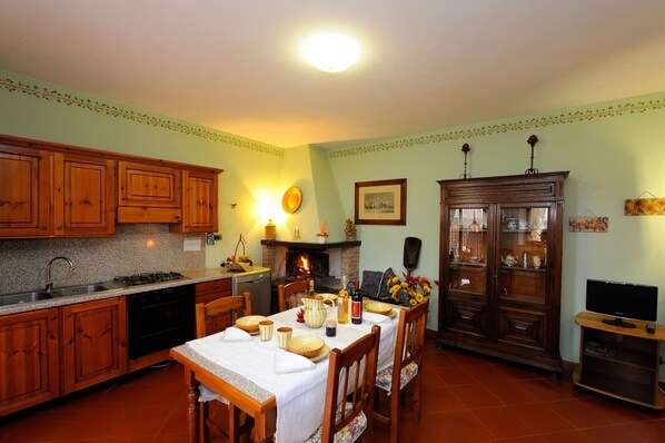 Une cuisine traditionnelle avec des meubles en bois, une table à manger pour quatre personnes, une cheminée et un téléviseur.