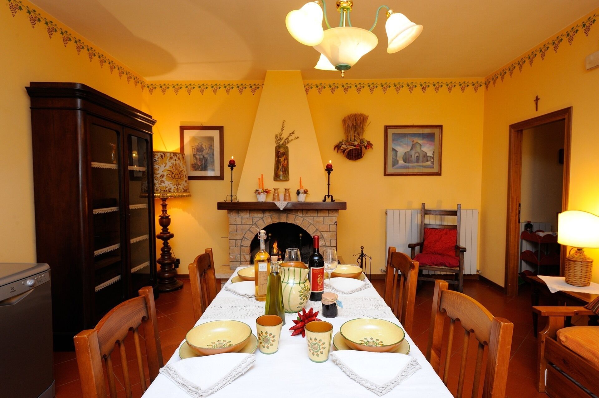Een eetkamer met een lange tafel voor zes personen, een open haard en een kroonluchter.