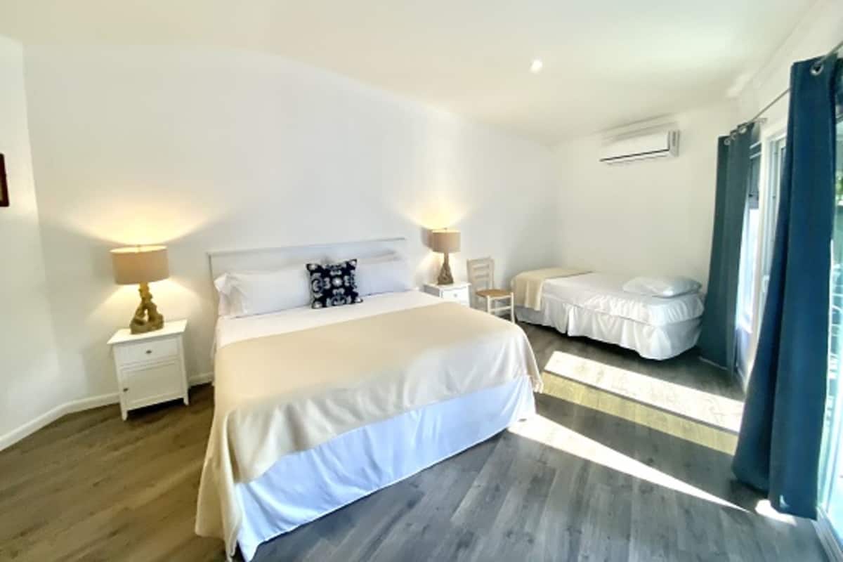 A bedroom with a large bed, two bedside tables, a chair, and a window with curtains.