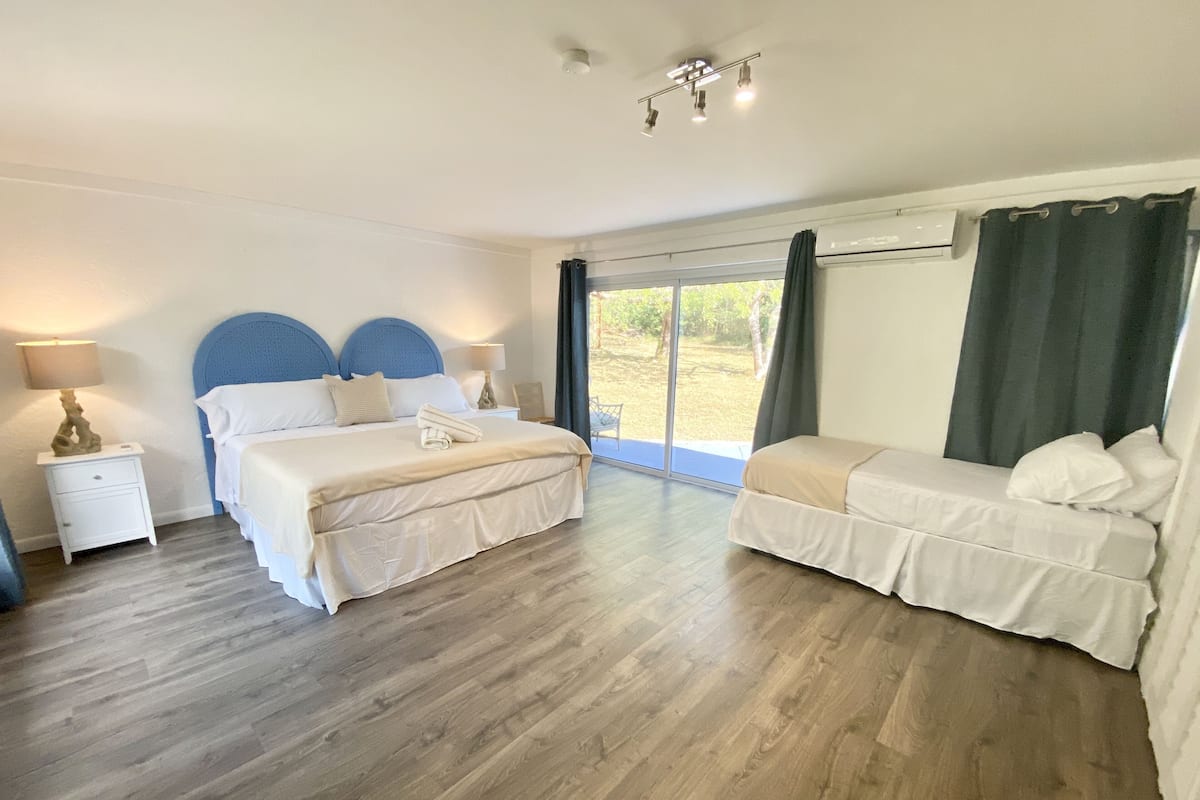 A bedroom with a bed, a sofa, a nightstand, and a window with curtains.