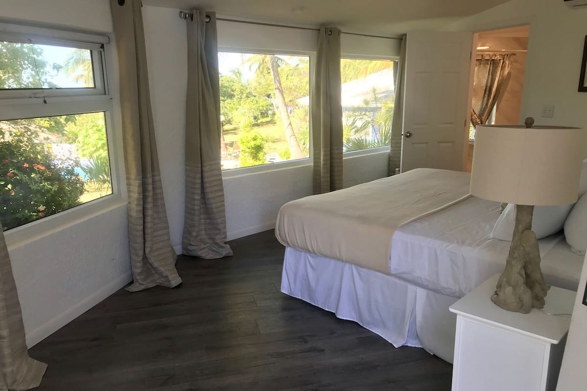 A bedroom with a bed, a nightstand, a lamp, and a view of greenery outside.