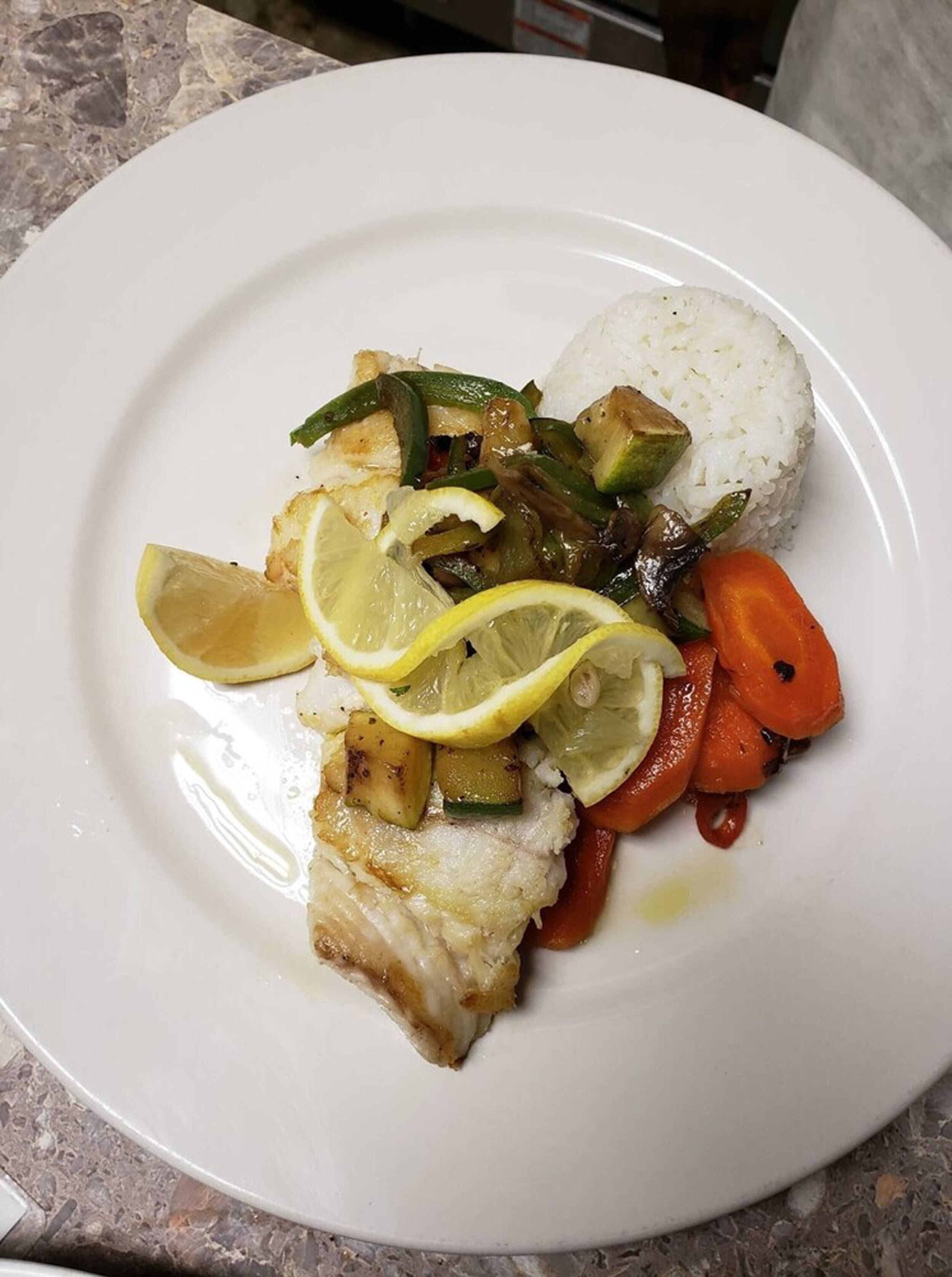A plate with white rice, grilled fish, and mixed vegetables including carrots and bell peppers.