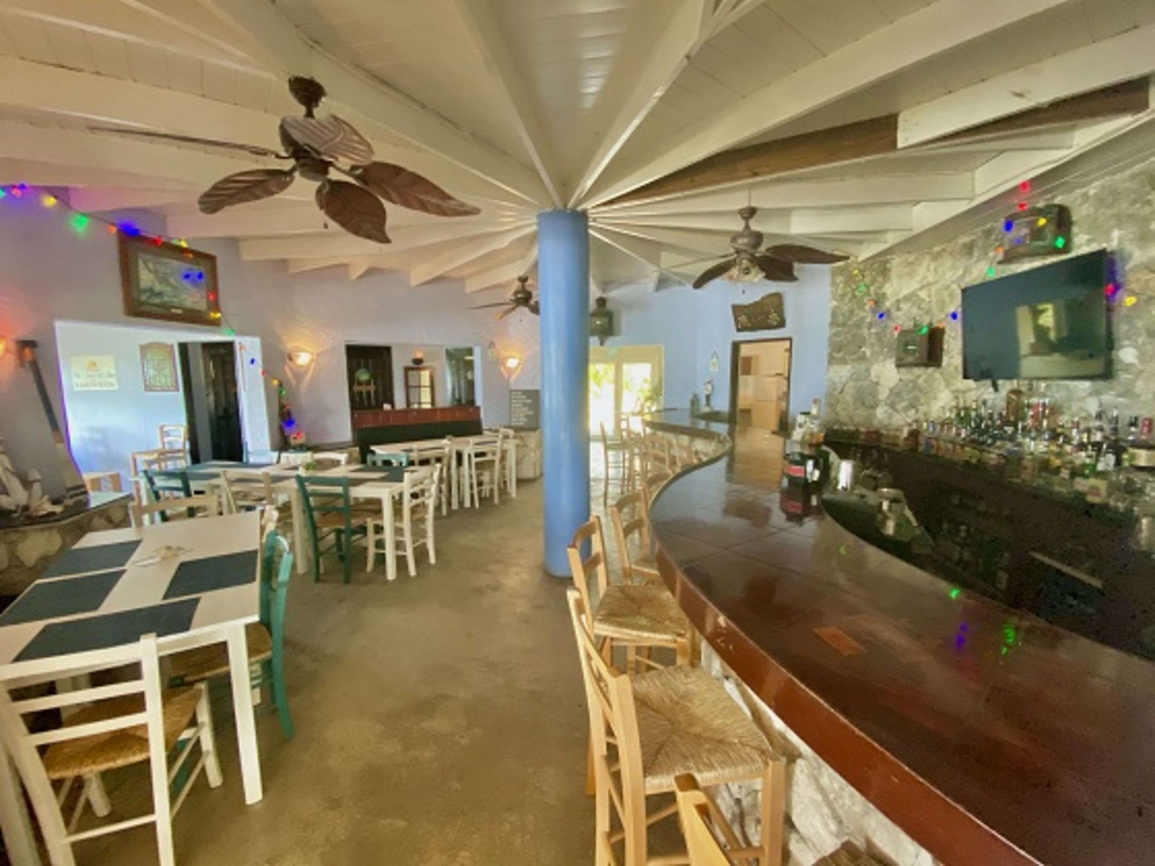 Eine Bar mit Holztischen und -stühlen, einer Theke mit Flaschen und Deckenventilatoren.