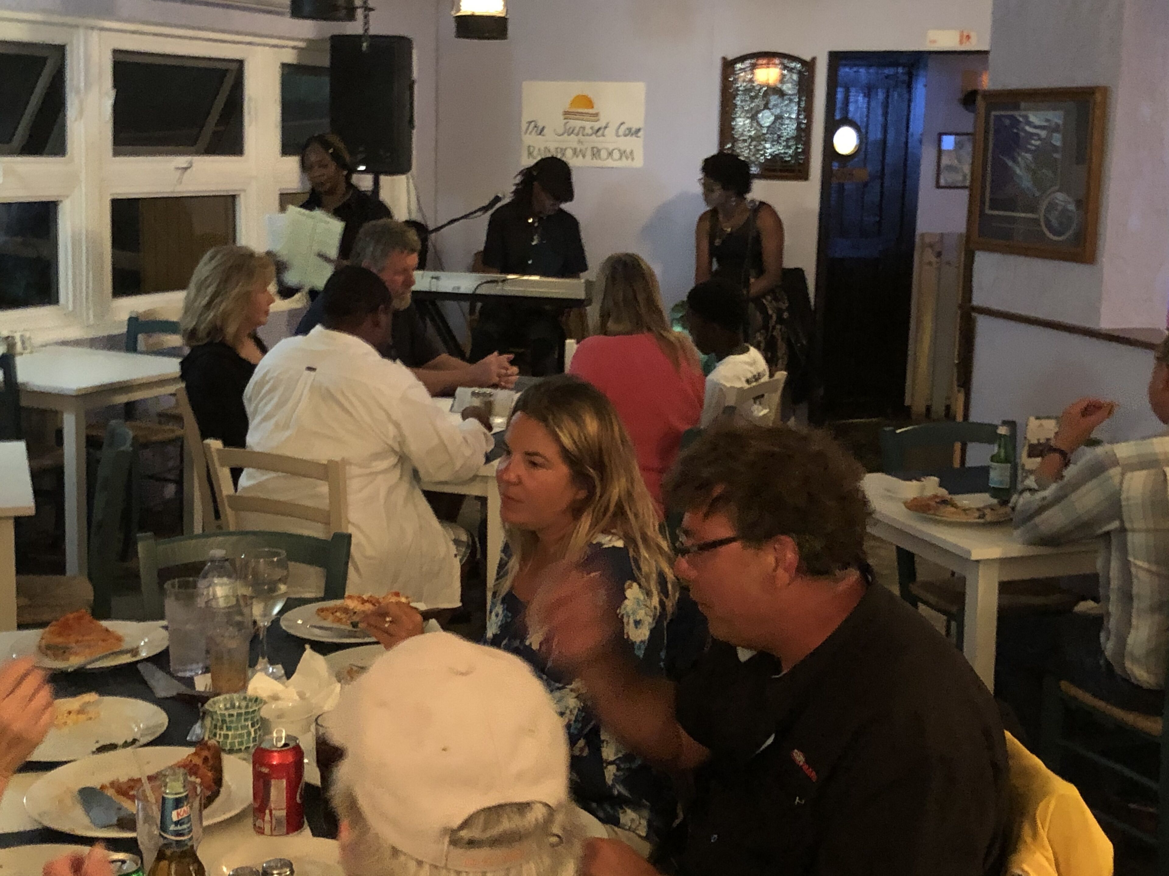 A restaurant with tables and chairs, a stage with a band, and a sign for 'The Sunset Cafe'.