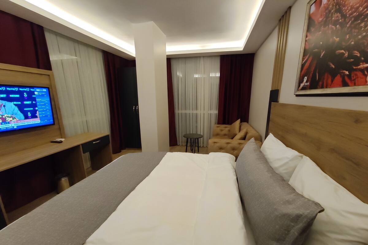 Ein Hotelzimmer mit Bett, Fernseher, Schreibtisch, Stuhl und einem Fenster mit Vorhängen.