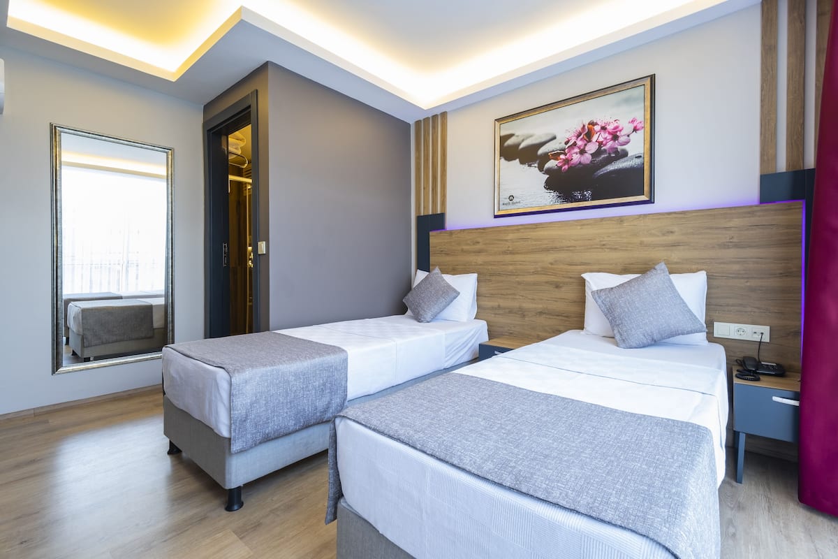 Ein Hotelzimmer mit zwei Einzelbetten, einem Holzkopfstück, einem großen Fenster und einem Bild an der Wand.