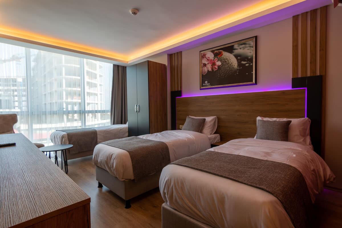 Ein modernes Hotelzimmer mit zwei Betten, einem kleinen Tisch und Blick auf eine Stadtkulisse durch große Fenster.