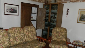 A living room with a brick ceiling, a wooden coffee table with a lace doily, floral-patterned sofas, a wooden cabinet with glass doors, and a framed picture on the wall. - Mamota B&B (Vesime)