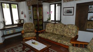 A cozy living room with a brick ceiling, a wooden coffee table, floral-patterned sofas, and a bookshelf filled with books. - Mamota B&B (Vesime)
