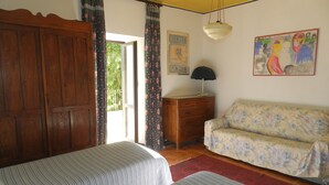 A room with a wooden wardrobe, a bed with striped bedding, a floral sofa, a small wooden dresser, and a hanging lamp. - Mamota B&B (Vesime)