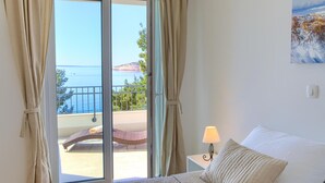 A bedroom with a bed, a nightstand, a lamp, and a view of the sea through a sliding glass door. - Lovely home in Martinscica (Martinscica)