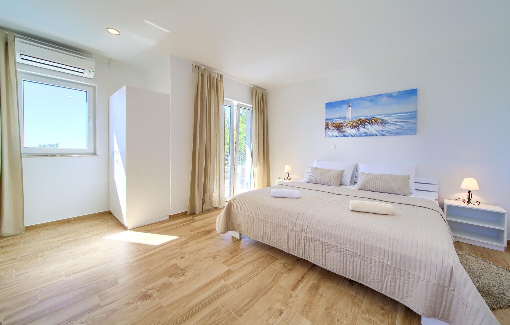 A bedroom with a large bed, a window, a painting, and a nightstand.