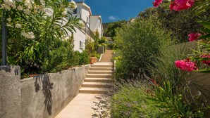 A narrow, concrete staircase leading up to a white building with shutters, surrounded by lush greenery and flowering plants. - Lovely home in Martinscica (Martinscica)