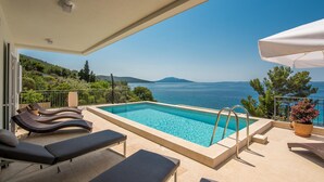 Zona de piscina con sillones de descanso, vista al mar y paisaje montañoso al fondo.