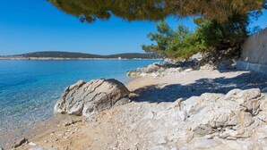 A rocky beach with clear blue water, a tree, and distant hills. - Lovely home in Martinscica (Martinscica)