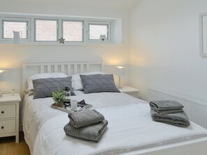 A neatly made bed with pillows, a bedside table with a lamp, a tray with towels, and a window with blinds.