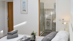 Ein Hotelzimmer mit einem Bett, einem Nachttisch mit Tablett voller Handtücher, einer Kaffeemaschine, einer Tasse und einem gerahmten Bild an der Wand.