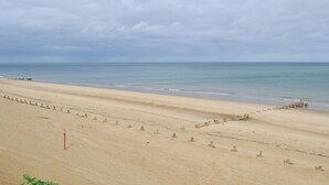 Ein weiter, sandiger Strand mit ruhiger See und bewölktem Himmel.