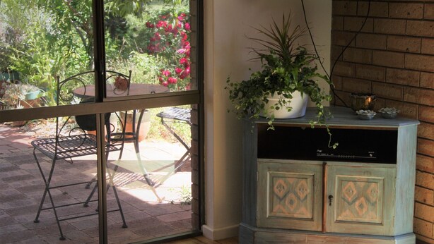 Una habitación con puerta corrediza de vidrio que da a un patio exterior. En el interior, hay un armario de madera con diseños decorativos y una planta en maceta encima.