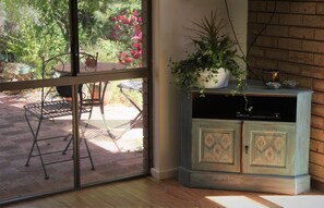 Una stanza con una porta a vetri scorrevoli che dà su un patio esterno. All'interno, si trova un mobiletto in legno con decorazioni e una pianta in vaso sopra.