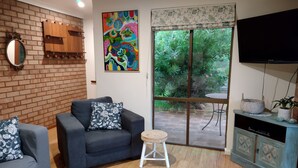 Una sala de estar con pared de ladrillo, un sofá, una mesa de centro, un televisor y un ventanal corredera que da a un jardín.