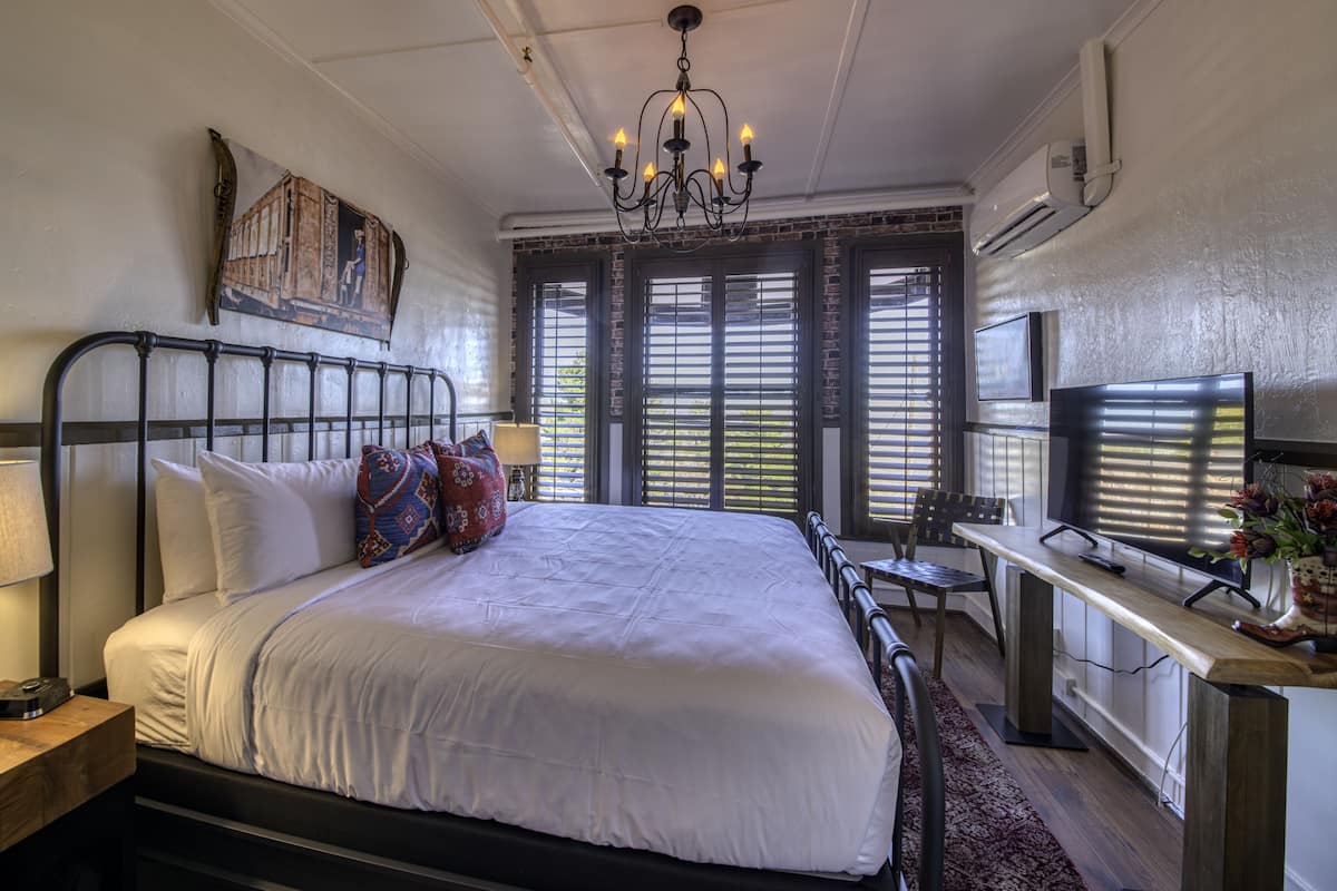 A bedroom with a large bed, a desk, a chair, a TV, and a chandelier.