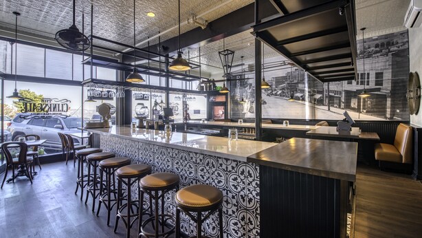 A bar area with a high counter, stools, and pendant lighting.