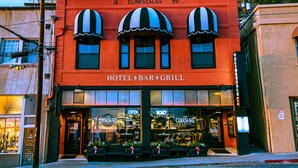 A hotel bar and grill with a red facade, numbered 18 and 99, and three large windows with striped awnings.
