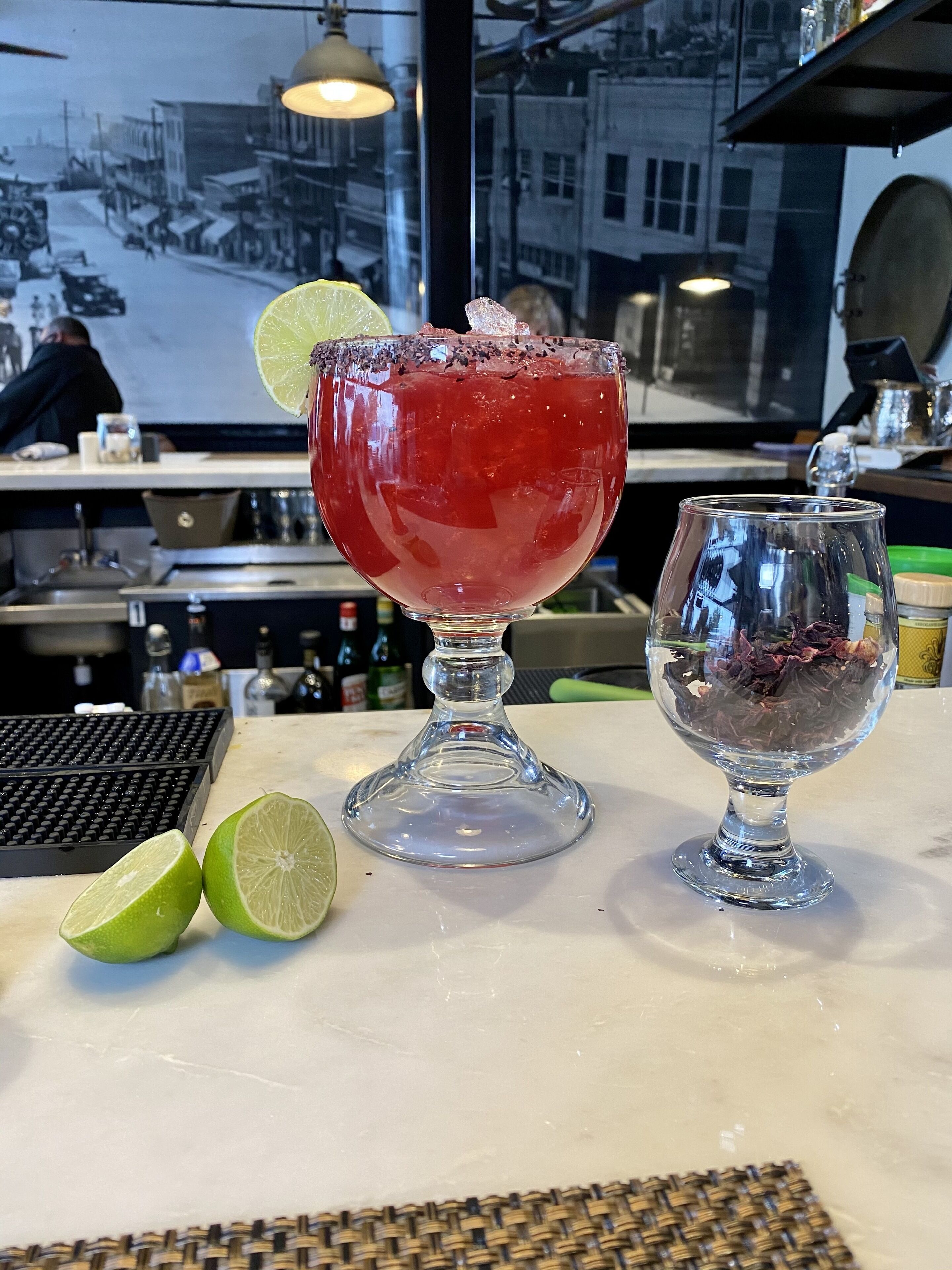 A bar setting with a cocktail glass, a lime wedge, and a small glass container with dried flowers.