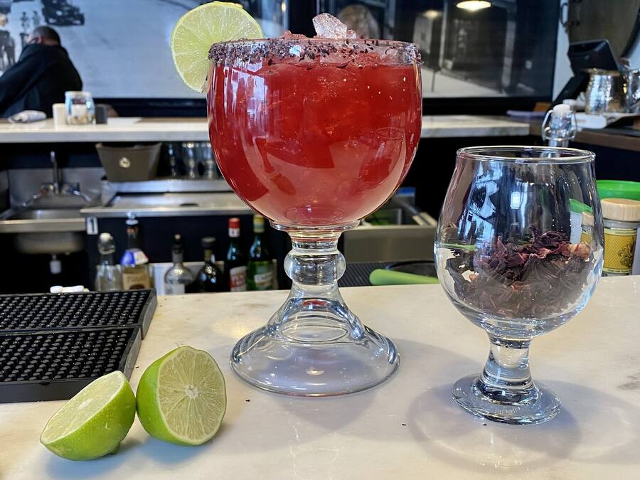 A bar setting with a cocktail glass, a lime wedge, and a small glass container with dried flowers.