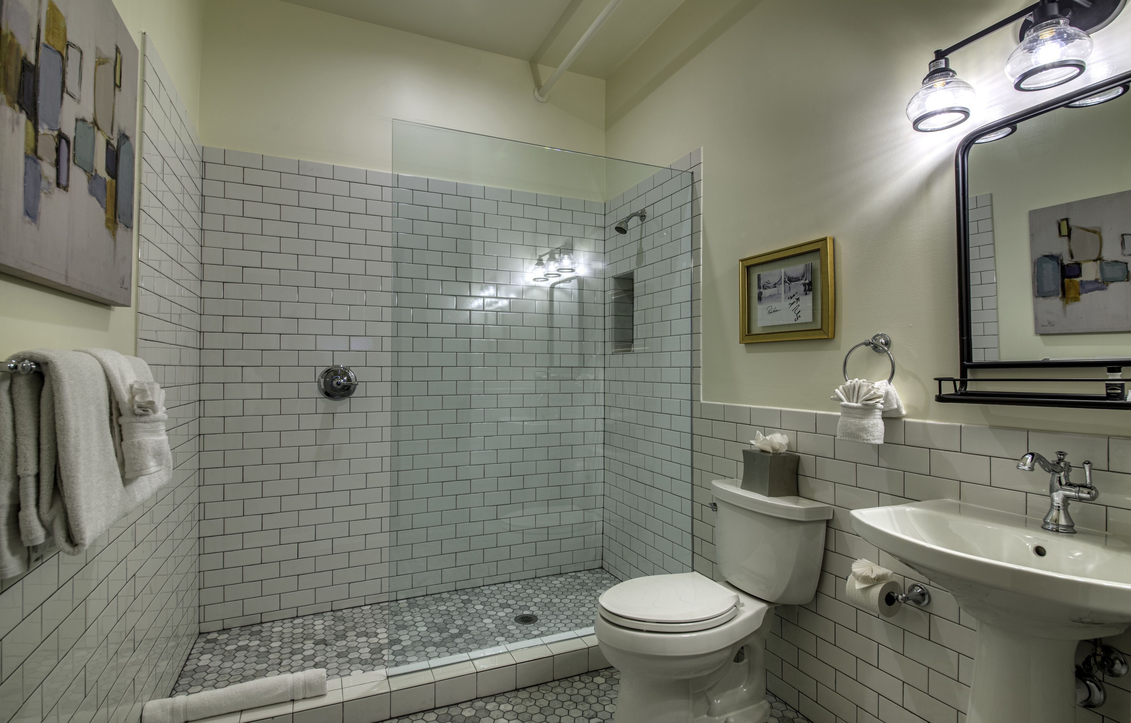 A bathroom with a glass-enclosed shower, white tiled walls, a toilet, and a sink with a mirror above it.