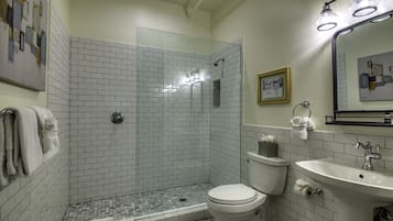 A bathroom with a glass-enclosed shower, white tiled walls, a toilet, and a sink with a mirror above it.