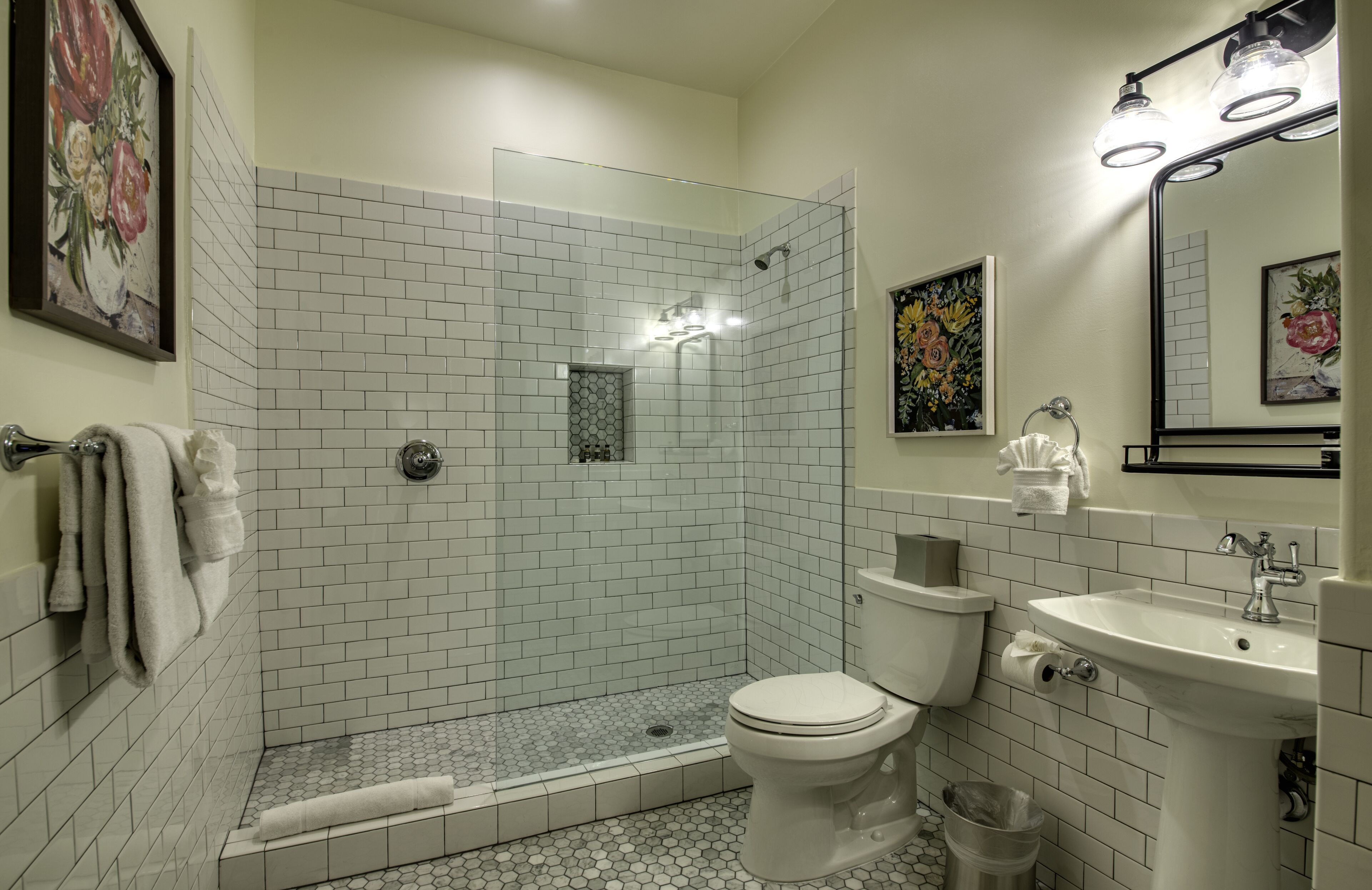 Un baño con ducha envuelta en vidrio, azulejos blancos, inodoro, lavabo y espejo.