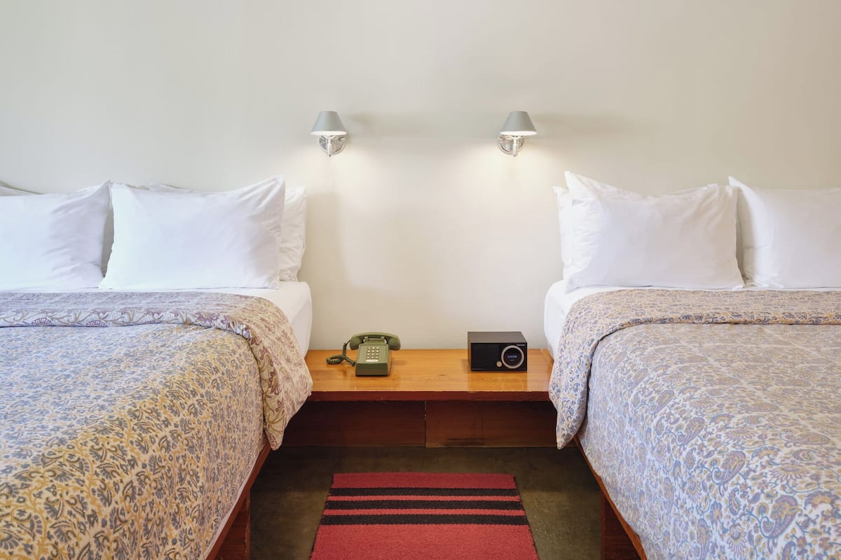 A hotel room with two beds, a bedside table with a telephone and a radio, and two wall-mounted lamps.