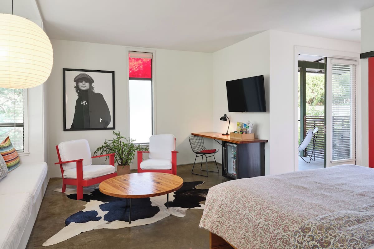 A modern bedroom with a bed, a desk with a computer, a chair, a sofa, a rug, and a television.