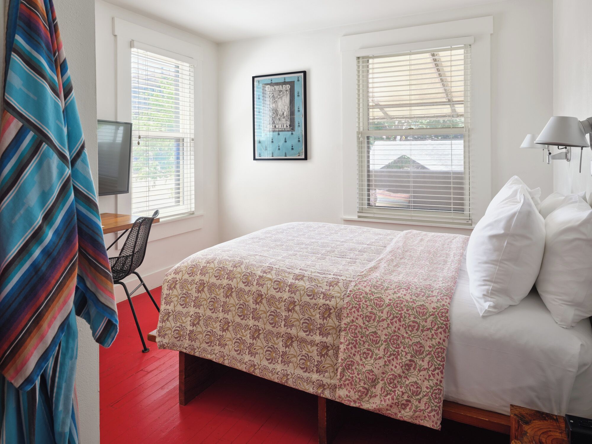 Un dormitorio con cama, una silla, un televisor y una ventana con persianas.